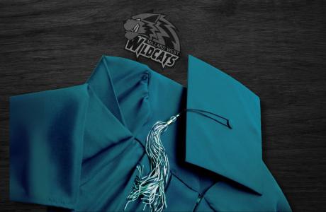 Green graduation cap and gown and a wildcat logo laying on a black wood surface