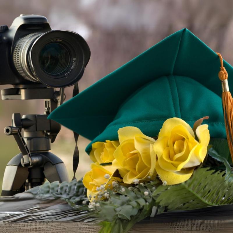 Image of a camera pointed at a green graduation cap sitting on yellow roses