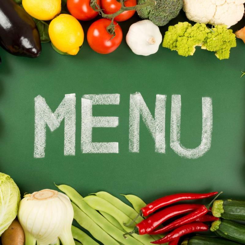 Green chalkboard with MENU written in chalk surrounded by fruits and vegetables